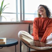 Eine junge Frau sitzt zuhause auf einem Stuhl und lacht Eine junge Frau sitzt zuhause auf einem Stuhl und lacht